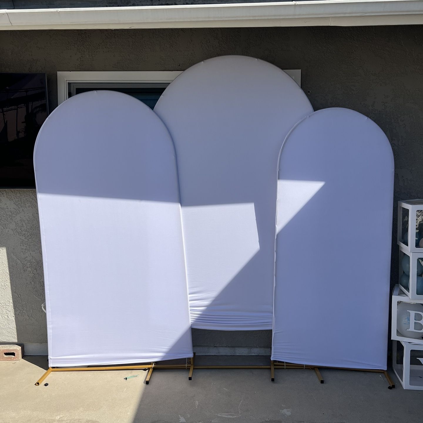 Set of three white arch backdrops with gold stands outdoors