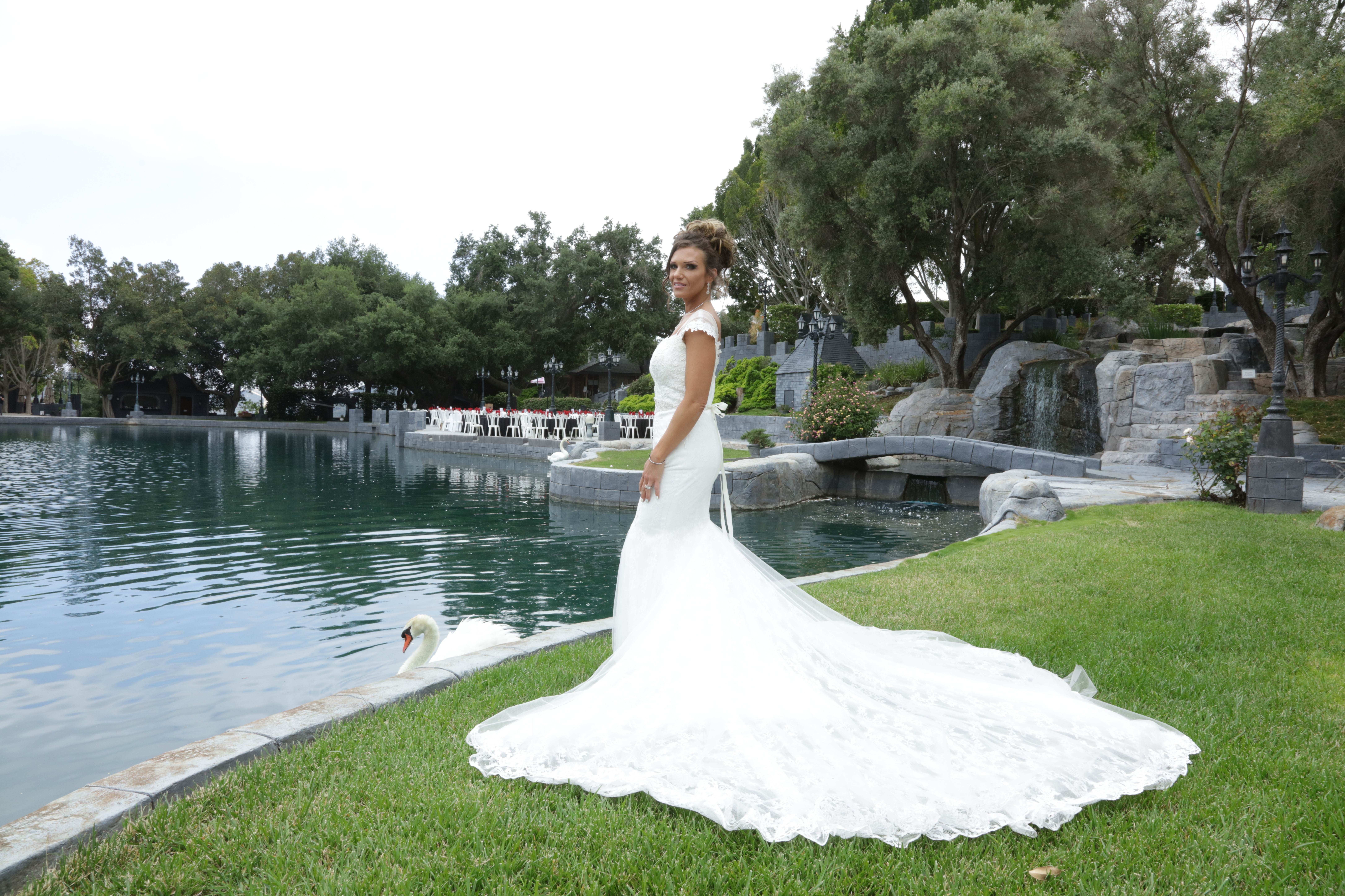Bride wearing a fitted lace wedding dress with a long train beside a lake
