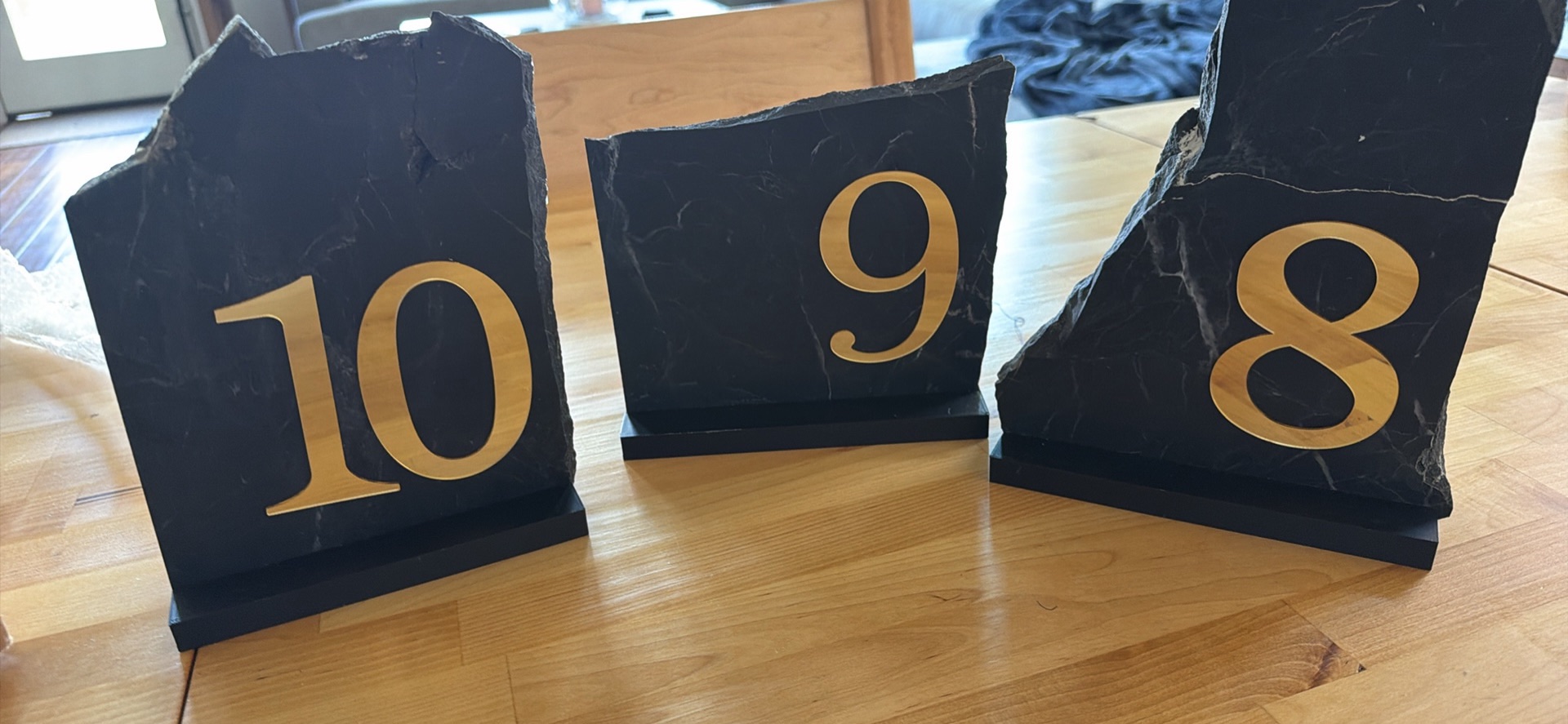 Black stone table numbers with gold numerals on a wooden table